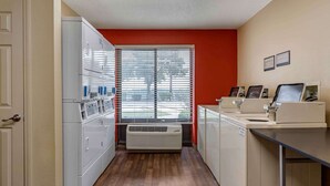 A laundry room with a row of washers and dryers, a large window with blinds, and a sign indicating the room's purpose. - Extended Stay America Suites Houston Med Ctr NRG Park Kirby (Houston)