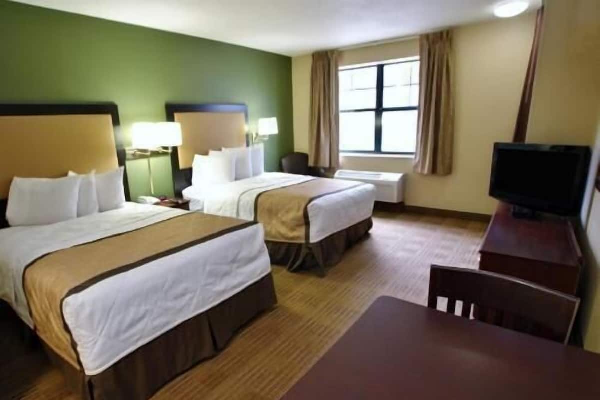 A hotel room with two beds, a desk, a chair, a television, and a window with curtains.