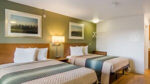 A hotel room with two beds, a nightstand with a lamp, and framed pictures on the wall. - Birch Hill Suites Sulphur (Sulphur)
