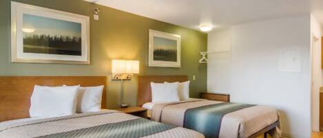 A hotel room with two beds, a nightstand with a lamp, and framed pictures on the wall.