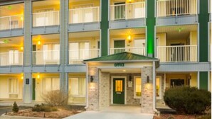 A multi-story hotel with a green and white facade, a stone entrance, and balconies with railings. - Birch Hill Suites Sulphur (Sulphur)