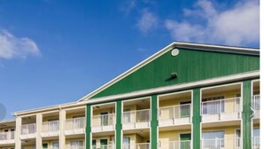A multi-story hotel with balconies, a green roof, and a clear blue sky. - Birch Hill Suites Sulphur (Sulphur)