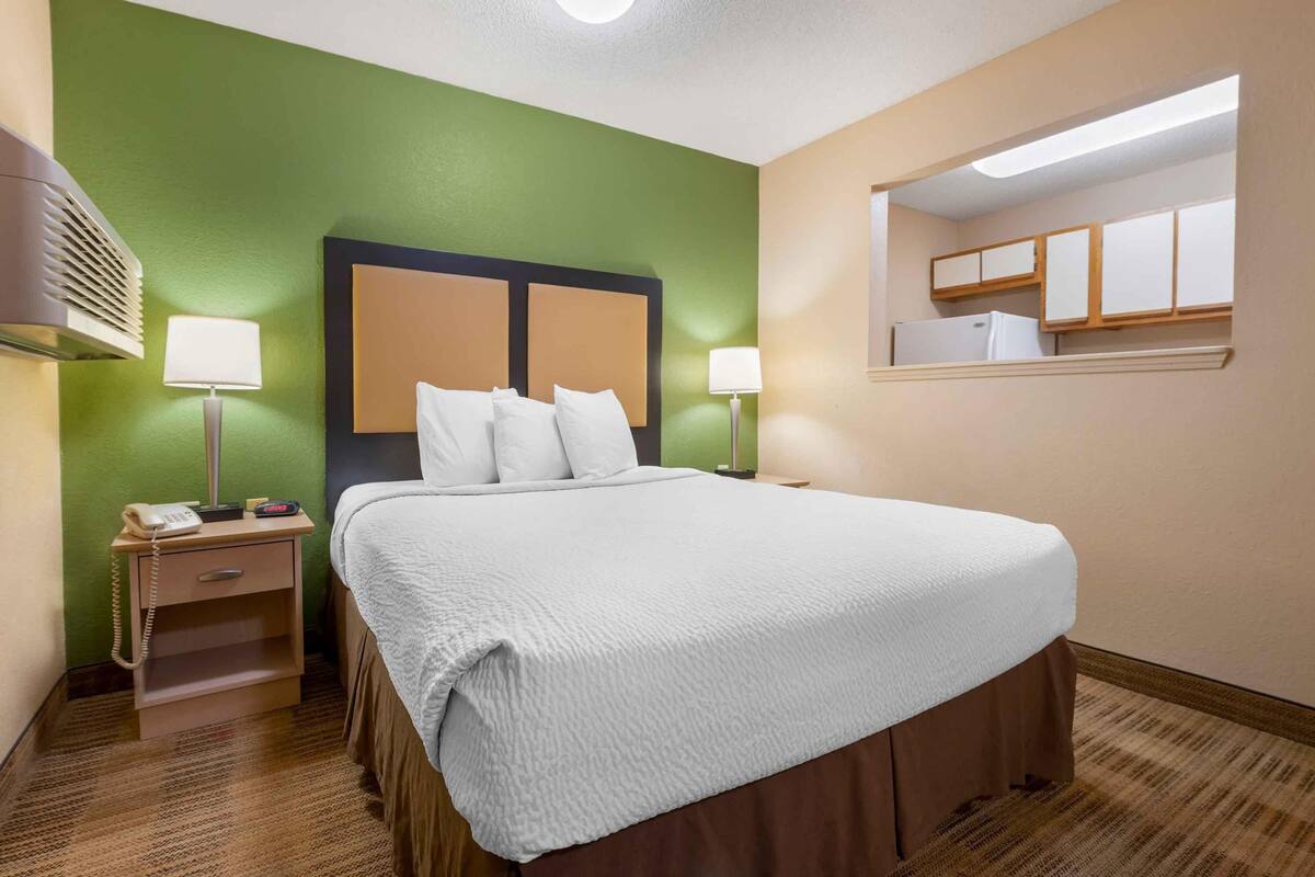 A hotel room with a large bed, two bedside tables, a nightstand, a mirror, and a small window.
