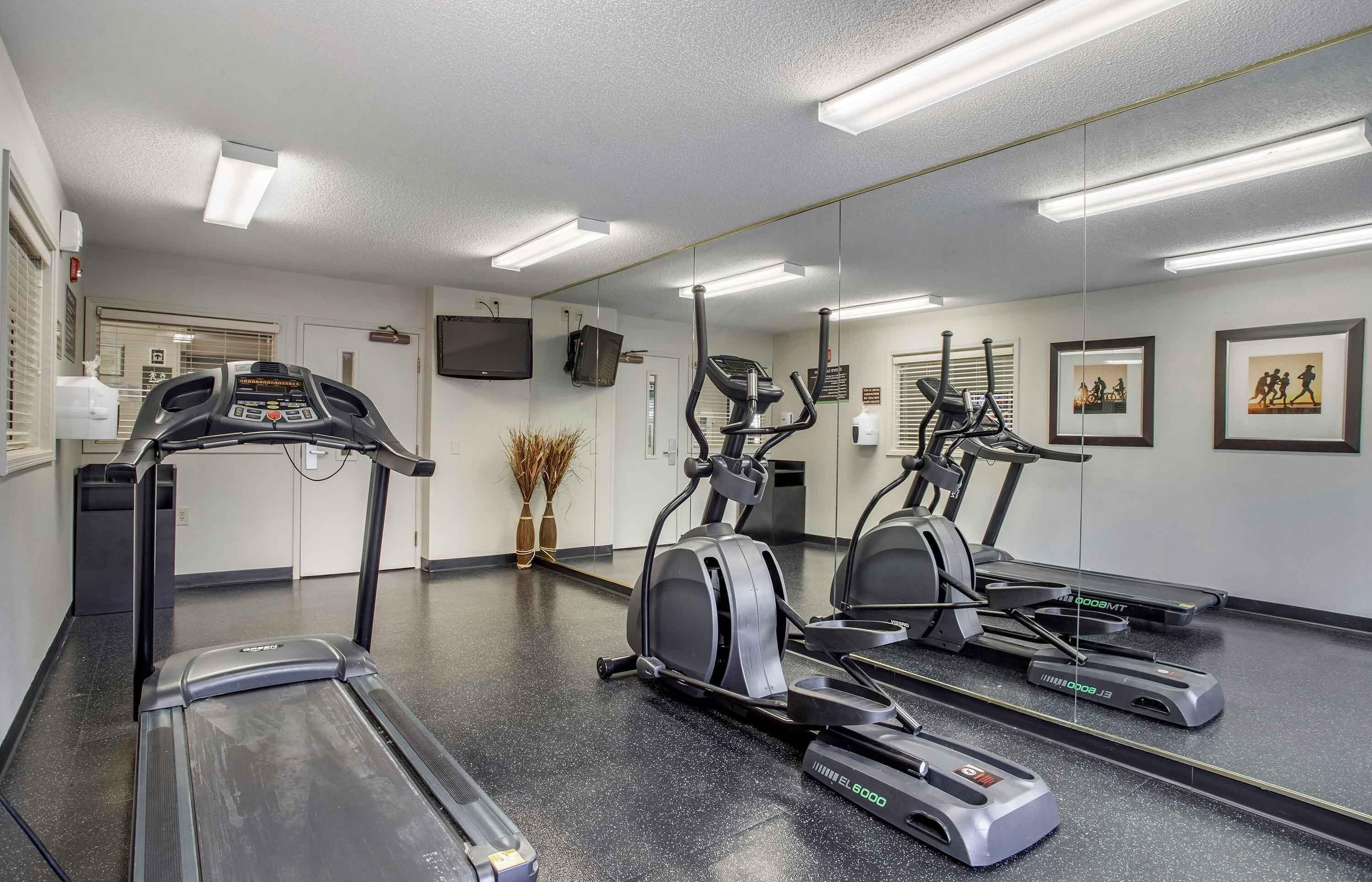 Une salle de sport équipée de tapis de course, de vélos elliptiques et d’un mur recouvert de miroirs.