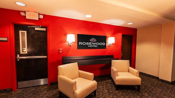 Un hall d’hôtel avec un mur rouge, un comptoir d’accueil, deux fauteuils et un panneau indiquant la sortie.