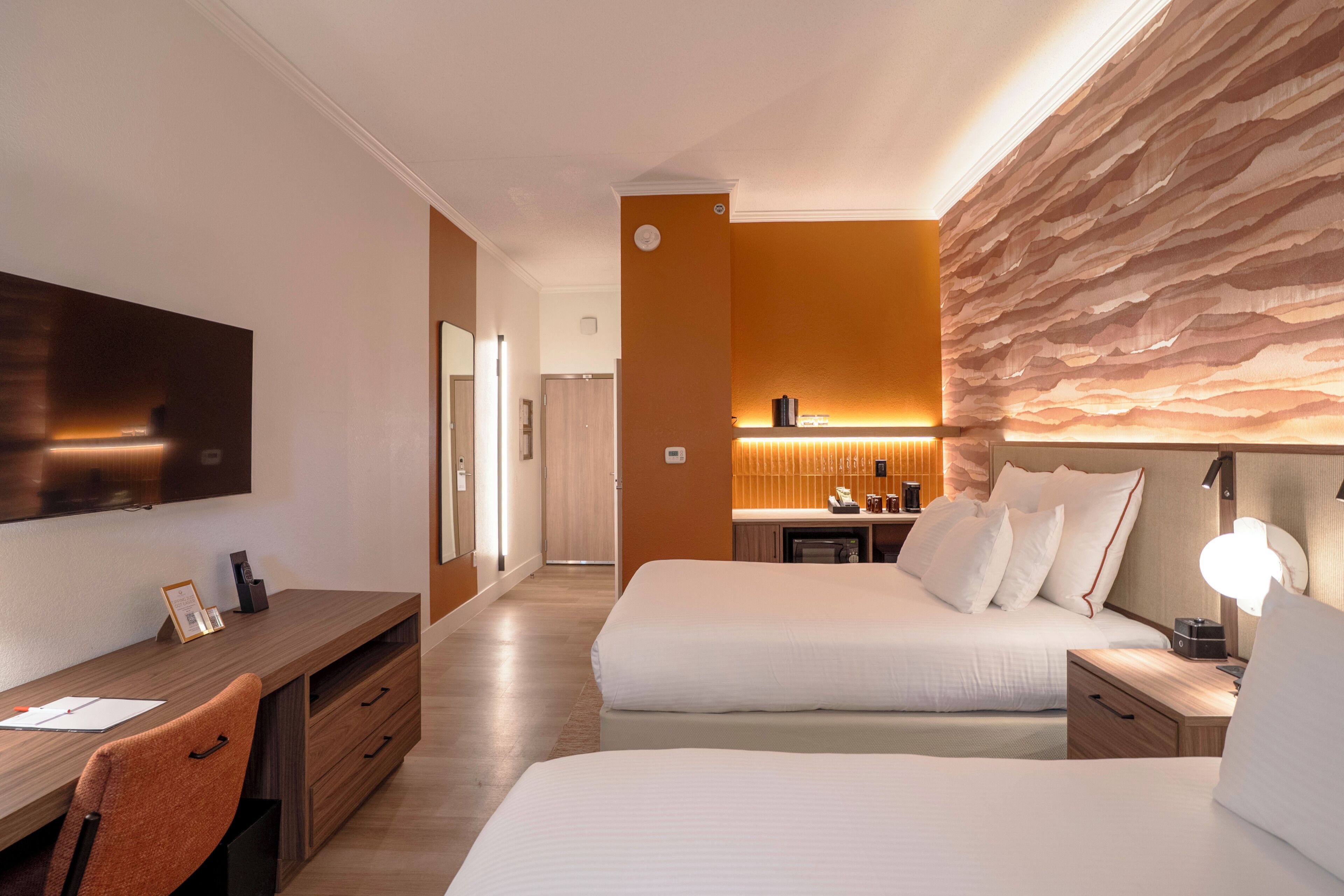 Una habitación de hotel con cama, mesita de noche, escritorio, silla y televisor.