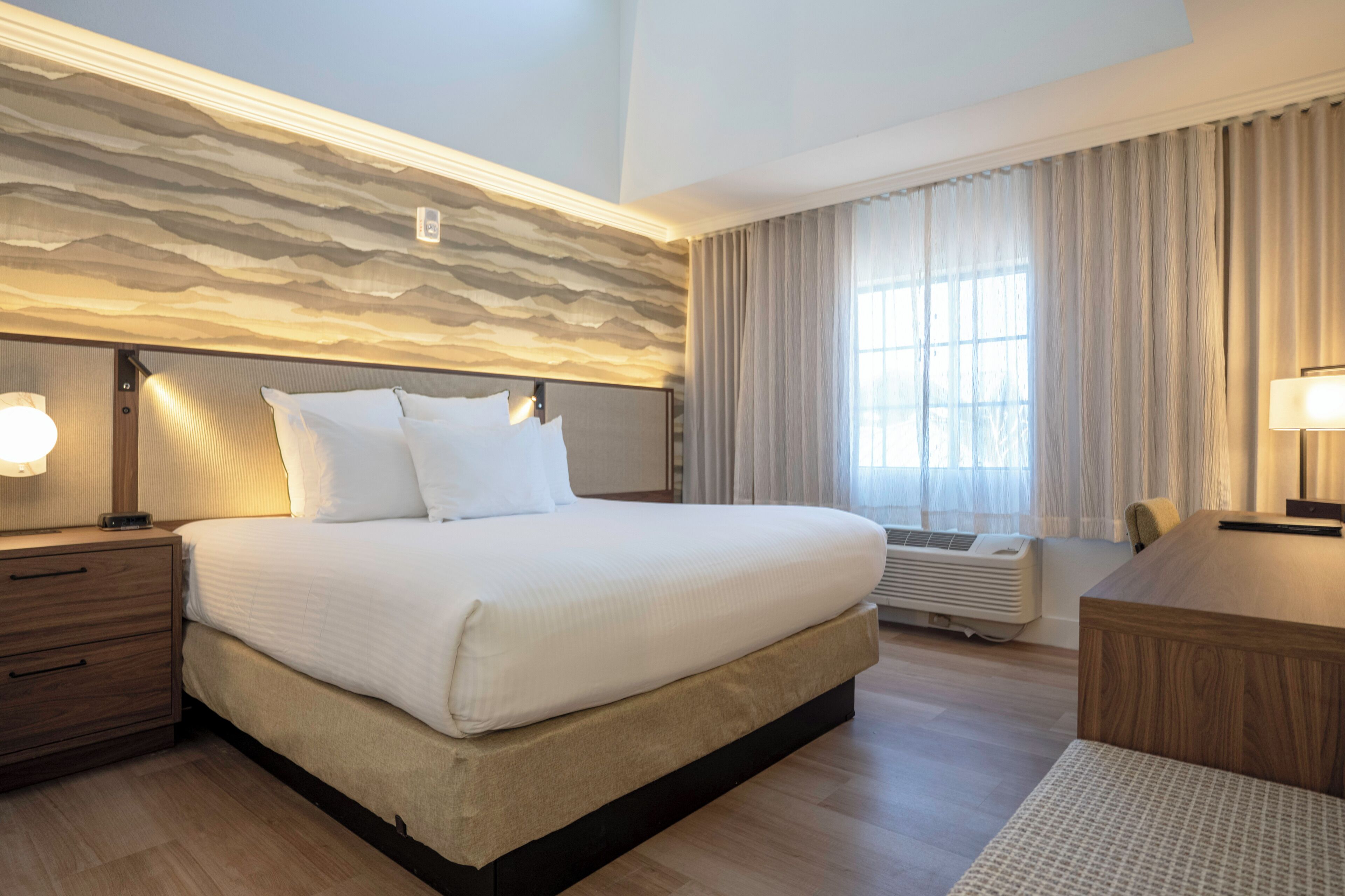 Une chambre d’hôtel avec un grand lit, des tables de chevet, un bureau et une fenêtre avec des rideaux.