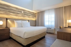 Habitación de hotel con una cama grande, mesitas de noche, un escritorio y una ventana con cortinas.