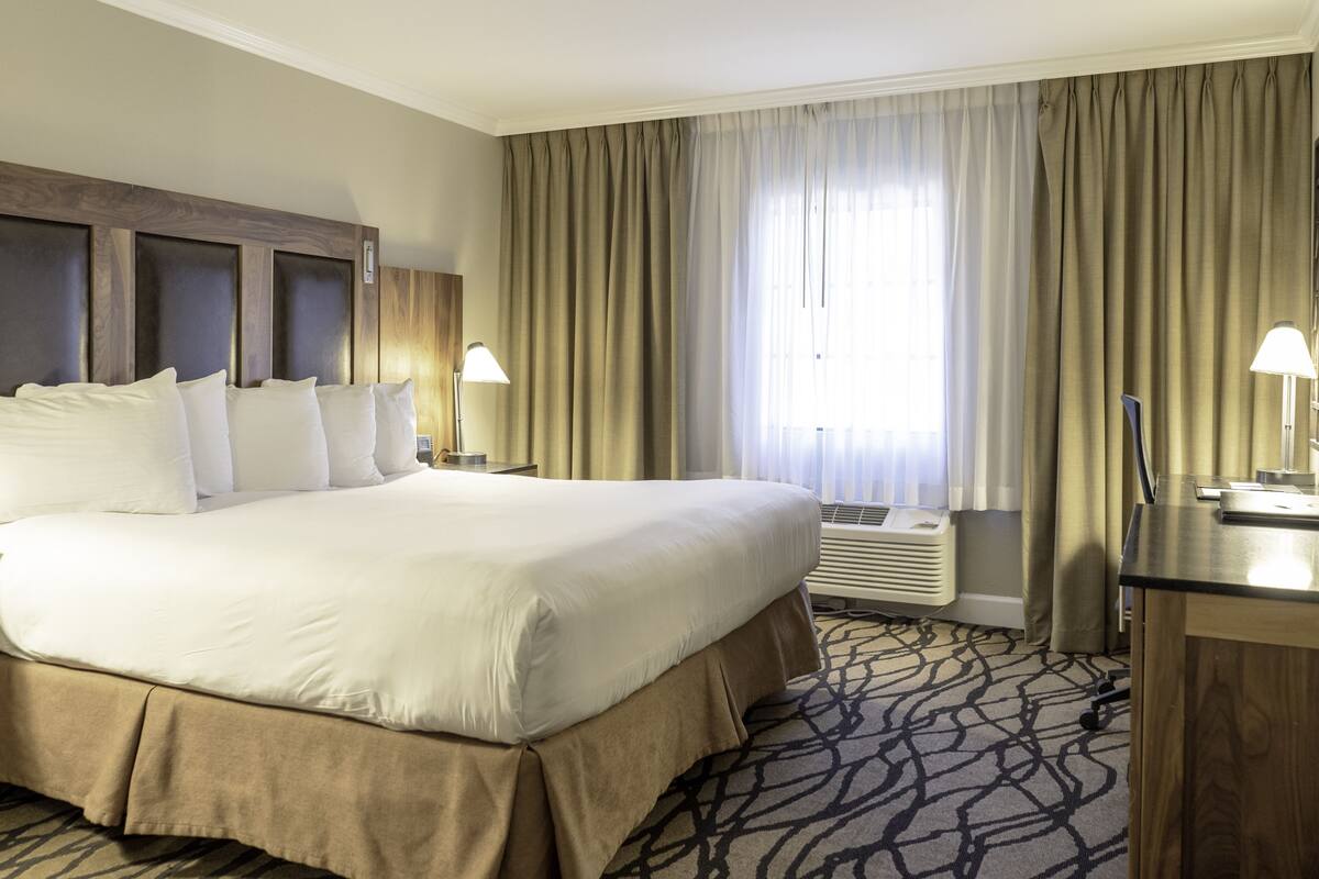 Una habitación de hotel con una cama grande, dos mesitas de noche con lámparas, un escritorio y una ventana con cortinas.