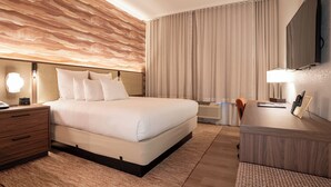 Ein Hotelzimmer mit einem großen Bett, einem Nachttisch, einem Schreibtisch und einem Spiegel.