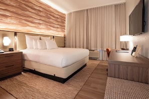 Una habitación de hotel con una cama grande, una mesita de noche, un escritorio y un espejo.