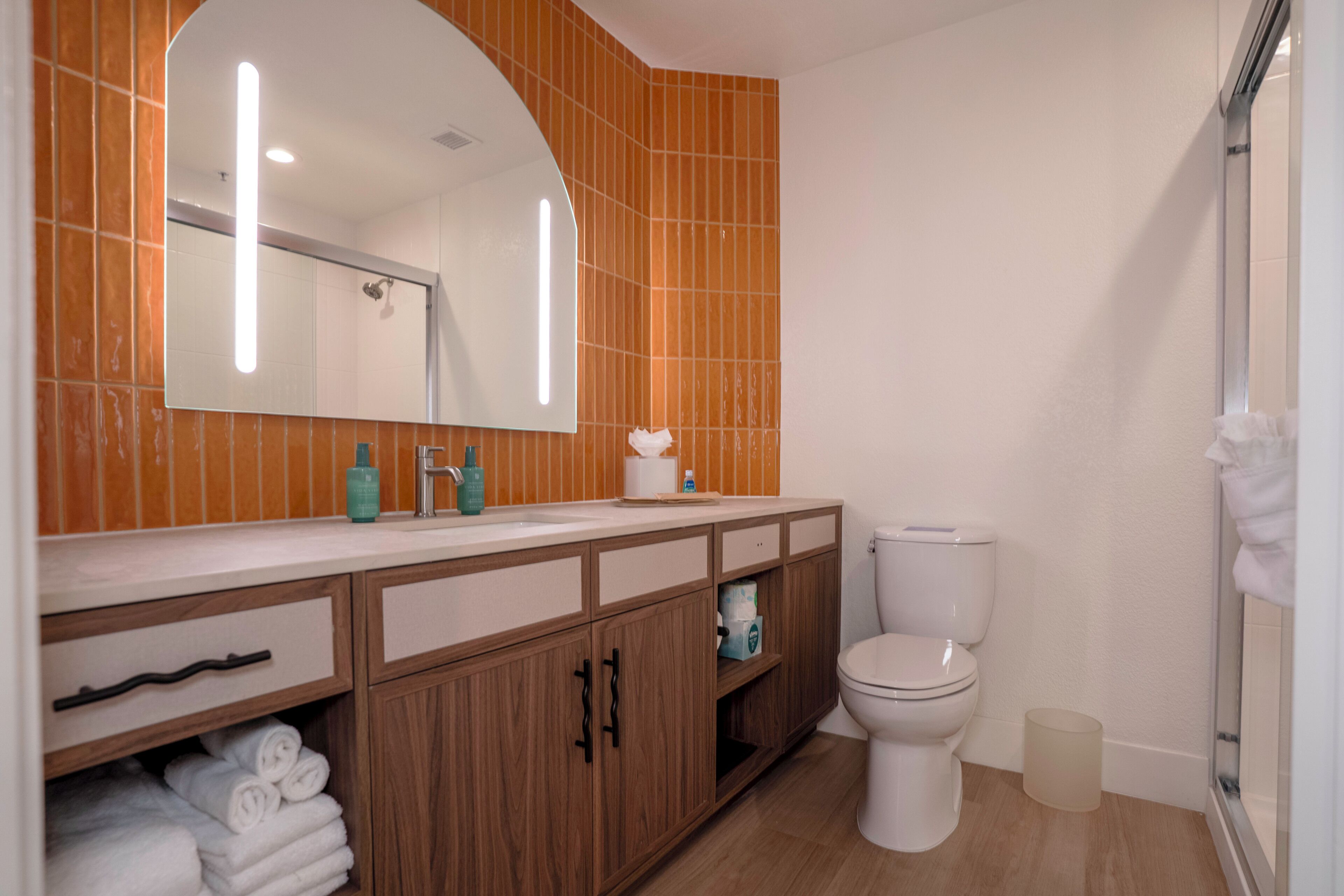A bathroom with a white toilet, wooden cabinets, a sink with a mirror, and a shower area.