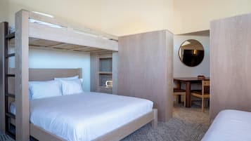 Une chambre d’hôtel avec un lit superposé, un bureau avec deux chaises et un miroir rond accroché au mur.