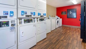 A laundry facility with multiple washing machines and dryers, a red wall with a framed picture, and a wooden floor. - Extended Stay America Select Suites Roanoke Airport (Roanoke)