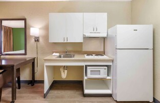 Una kitchenette compacta con gabinetes blancos, un lavamanos, un microondas y un refrigerador.