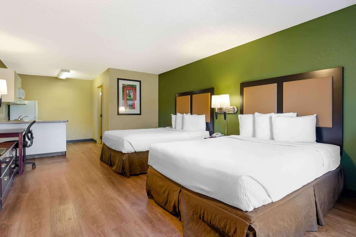 A hotel room with two beds, a desk, and a chair.