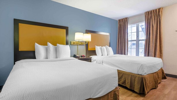 A hotel room with two beds, a nightstand with a lamp, a window with curtains, and a view of the outside. - Extended Stay America Select Suites Roanoke Airport (Roanoke)