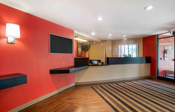 Un área de recepción con pared roja, mostrador de recepción, televisión de pantalla plana y suelo de madera.