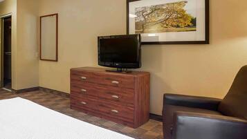 Una habitación de hotel con una cama, un aparador de madera, un televisor, un cuadro en la pared y una silla.
