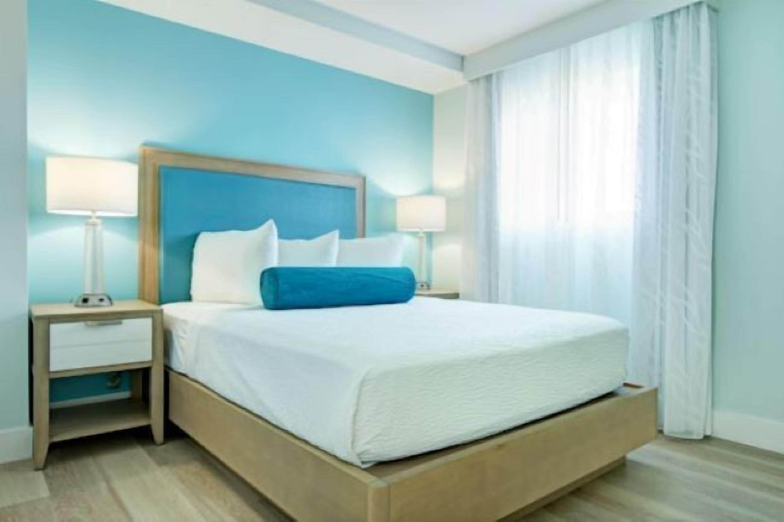 A hotel room with a single bed, two bedside tables, and a window with curtains.