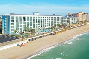 Un hotel con una fachada larga y moderna, un área de piscina y ubicación frente a la playa.