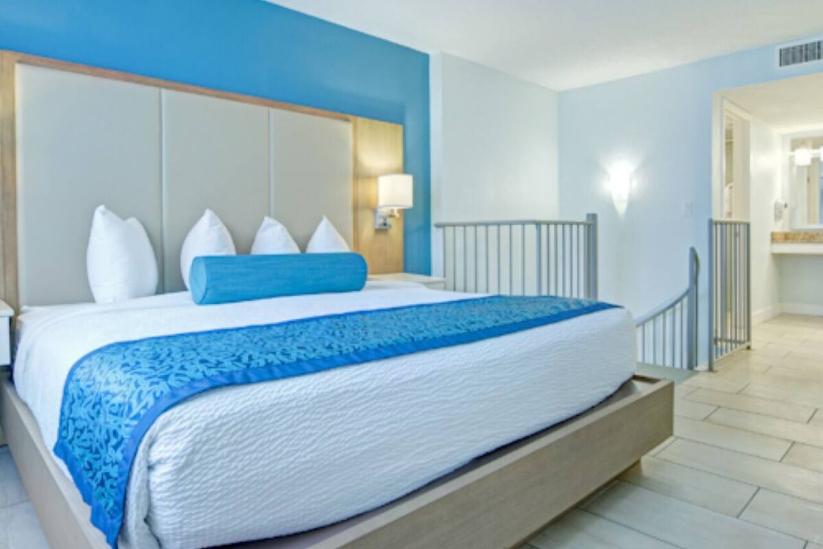 A bedroom with a large bed, a headboard, a nightstand, a lamp, and a view of a bathroom.