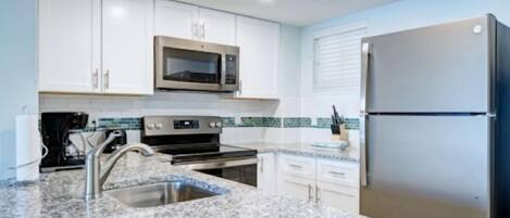 A modern kitchen with white cabinets, a stainless steel refrigerator, a microwave, and a granite countertop.