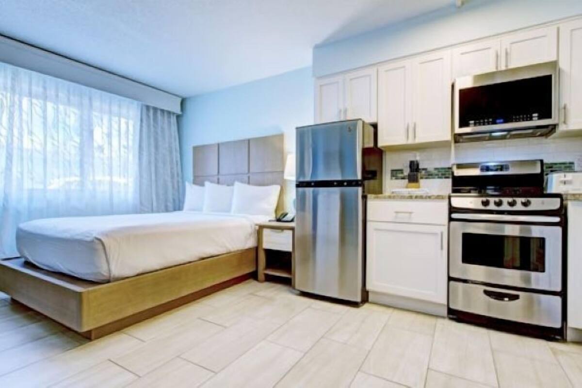 A modern hotel room with a bed, a refrigerator, a microwave, and a stove.