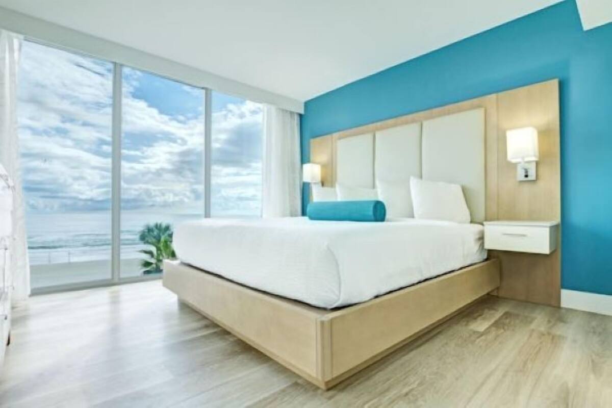 A modern bedroom with a large bed, a view of the ocean, and a blue accent wall.