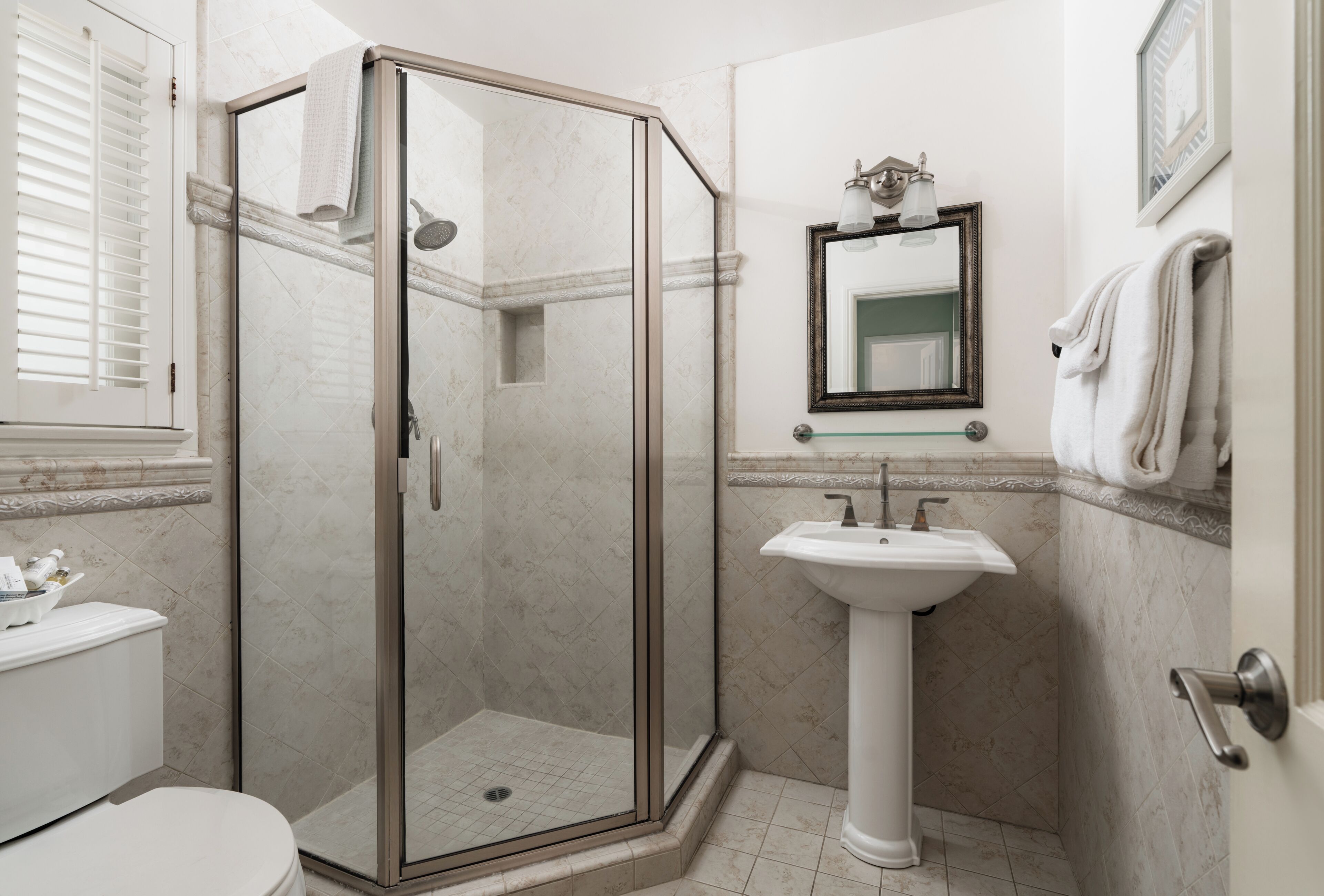 A bathroom with a glass-enclosed shower, a pedestal sink, and a toilet.