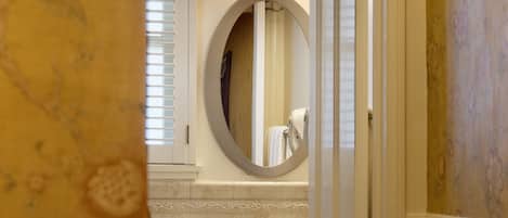 Un baño con un lavamanos pedestal, un espejo redondo y una lámpara fijada a la pared.