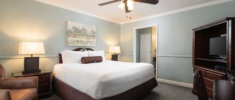 A hotel room with a bed, two bedside lamps, a ceiling fan, a TV, a desk, and a chair.