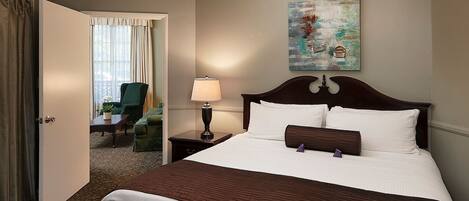 A hotel room with a bed, a nightstand, a lamp, a chair, and a painting on the wall.