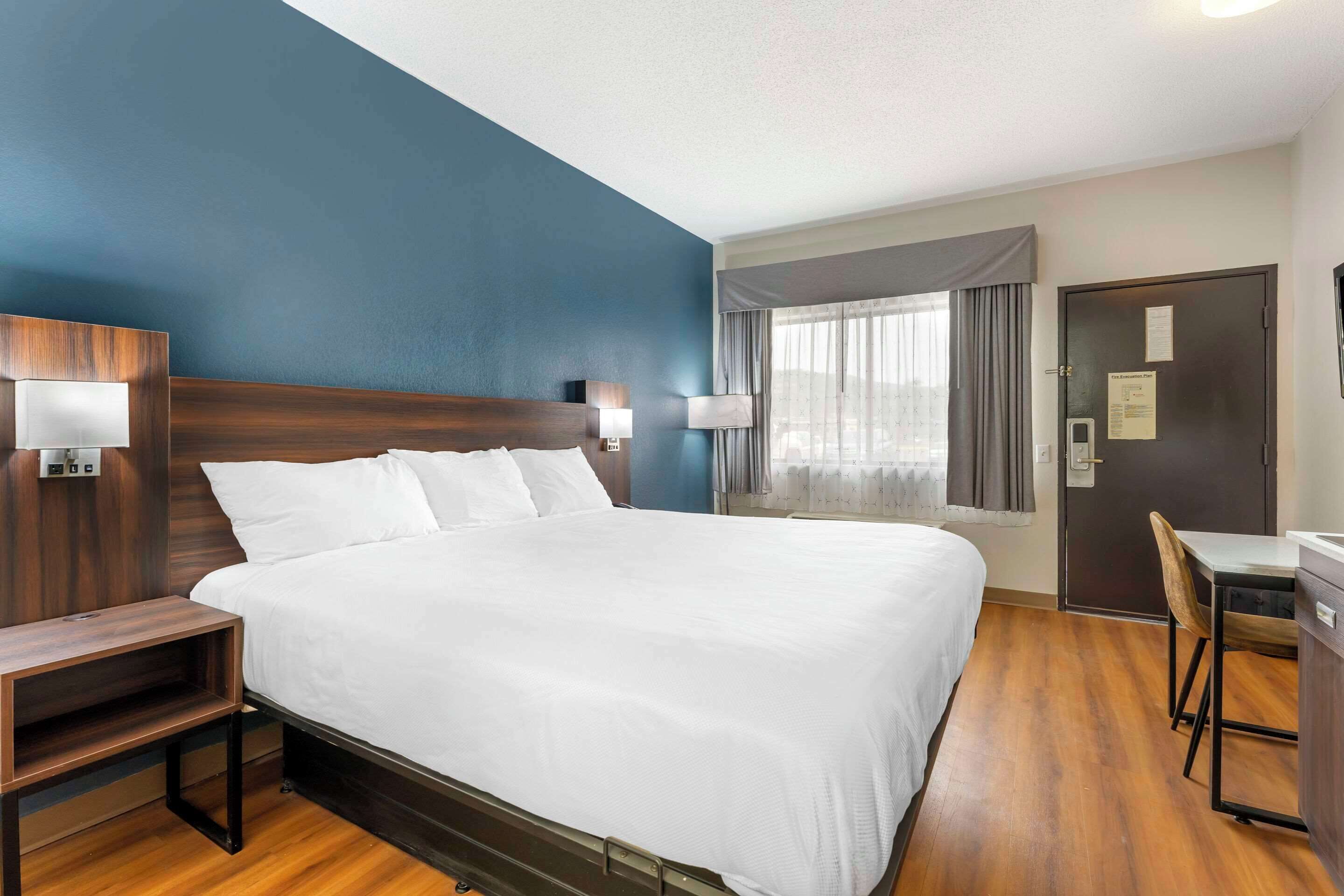 Une chambre d’hôtel avec un grand lit, des tables de chevet, un bureau avec une chaise et une fenêtre avec des rideaux.