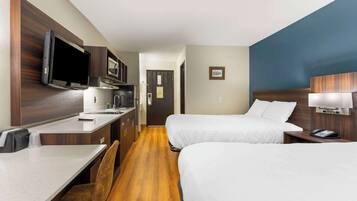 Quarto de hotel com duas camas, uma cozinha compacta, televisão e piso de madeira.