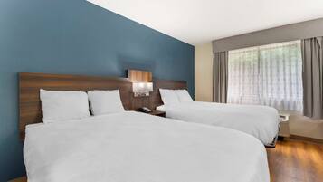 Habitación de hotel con dos camas, una mesita de noche, una lámpara y un ventanal con cortinas.