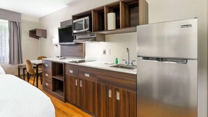 A compact kitchen with a microwave, refrigerator, and wooden cabinets. - Suburban Studios LaVale-Cumberland (Cumberland)