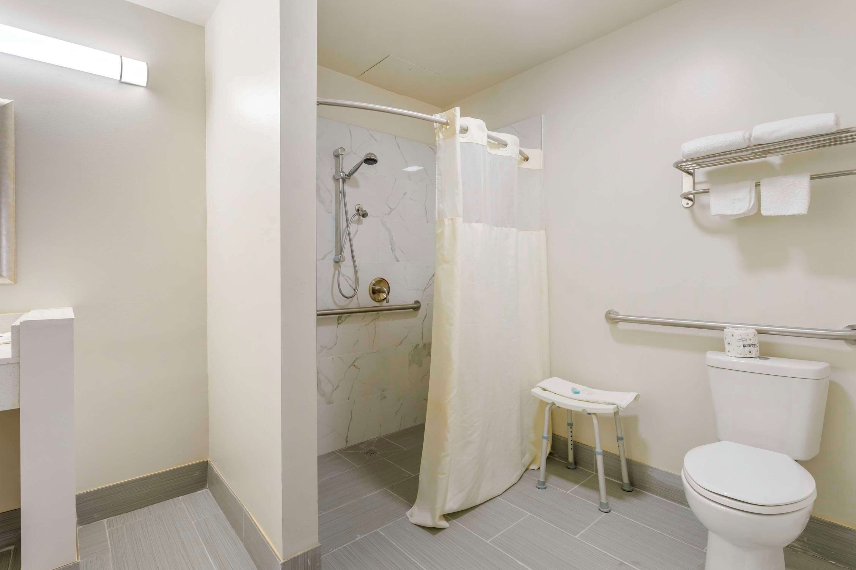 A bathroom with a shower, toilet, and a small table with a towel rack.