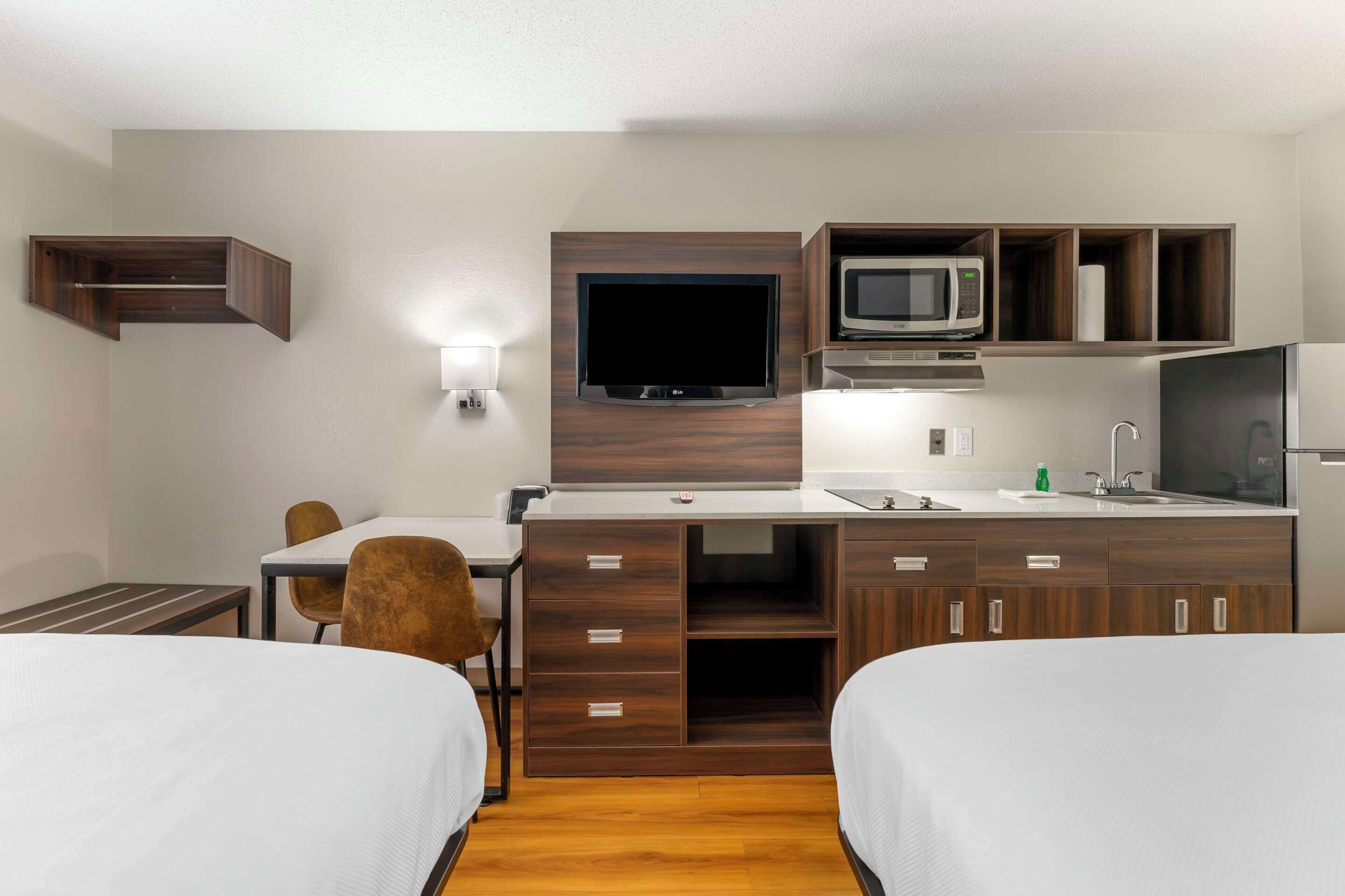 A compact hotel room with a kitchenette, a flat-screen TV, a microwave, a sink, and two beds.