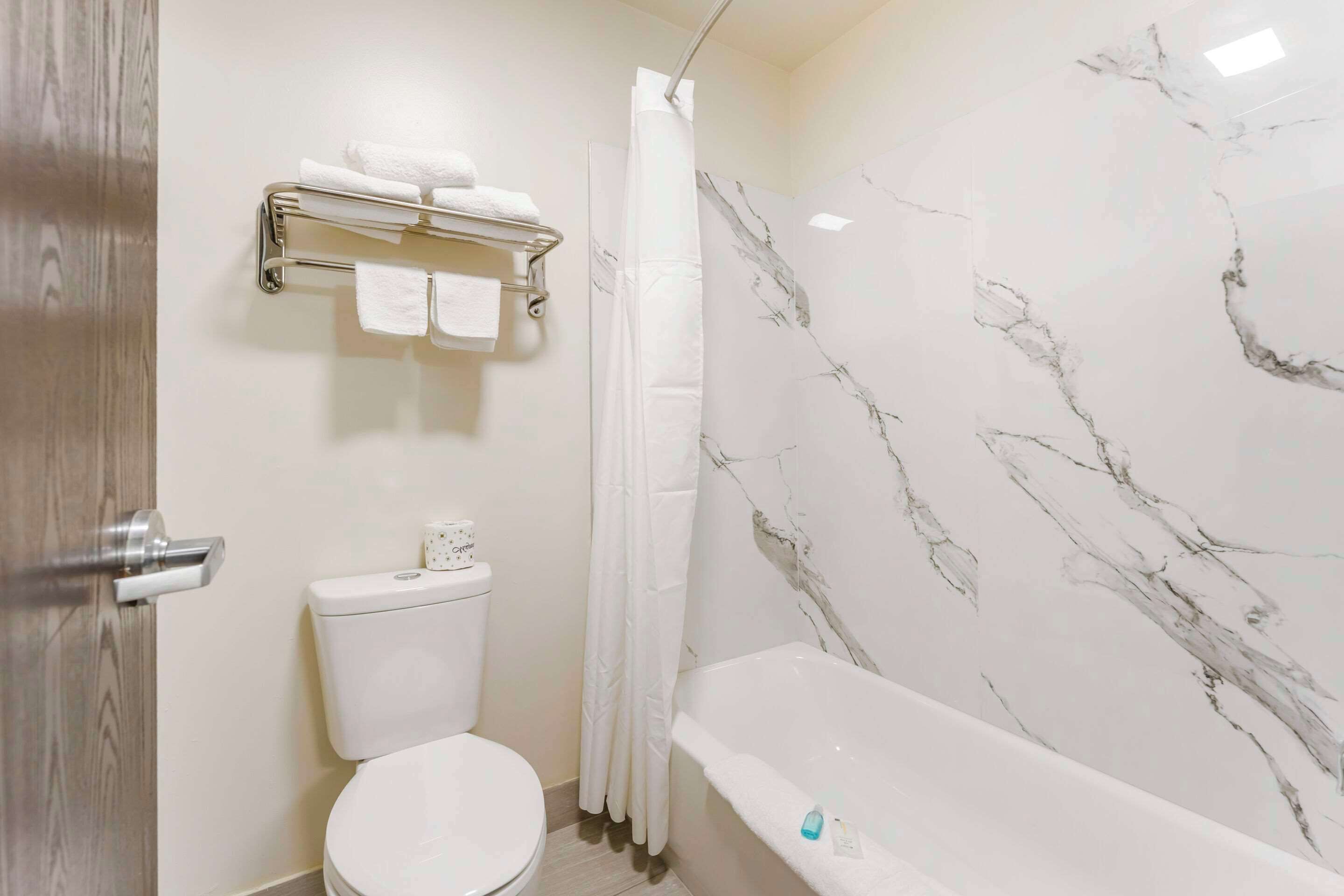 A bathroom with a toilet, a shower with a curtain, and a bathtub with a marble wall.