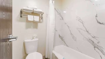 A bathroom with a toilet, a shower with a curtain, and a bathtub with a marble wall.