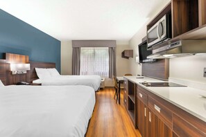 A hotel room with two beds, a kitchenette, a microwave, and a large window with curtains.