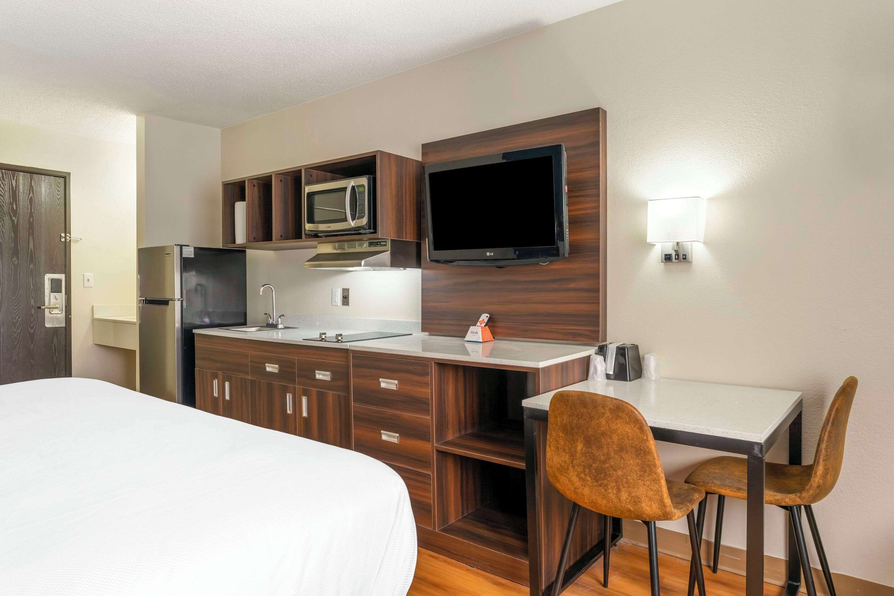 Habitación de hotel compacta con cama, kitchenette y una pequeña zona de comedor con mesa y dos sillas.