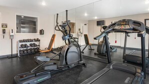 Un gimnasio con máquinas de cardio, pesas y un espejo grande.