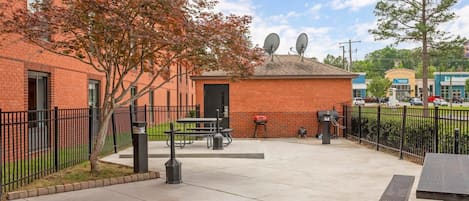 An outdoor patio area with picnic tables, a barbecue grill, and a trash can.