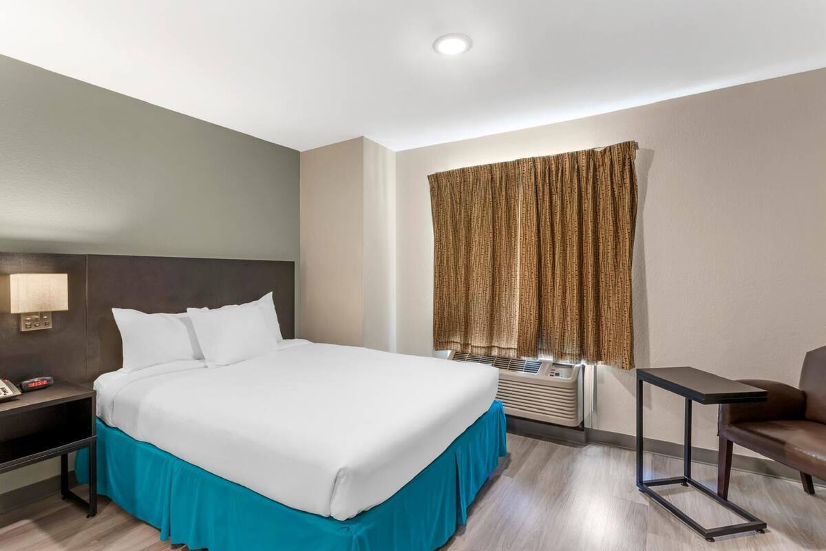 Una habitación de hotel con una cama grande, un escritorio, una silla y una ventana con cortinas.