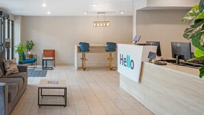 Una moderna zona de recepción con un cartel que dice 'Hello', dos sillones azules, un mostrador con computadoras y un sofá con una mesita de centro.