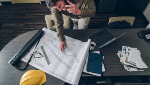 A man working at a desk with architectural plans, a laptop, and various office supplies. - Candlewood Suites Alexandria West by IHG (Alexandria)