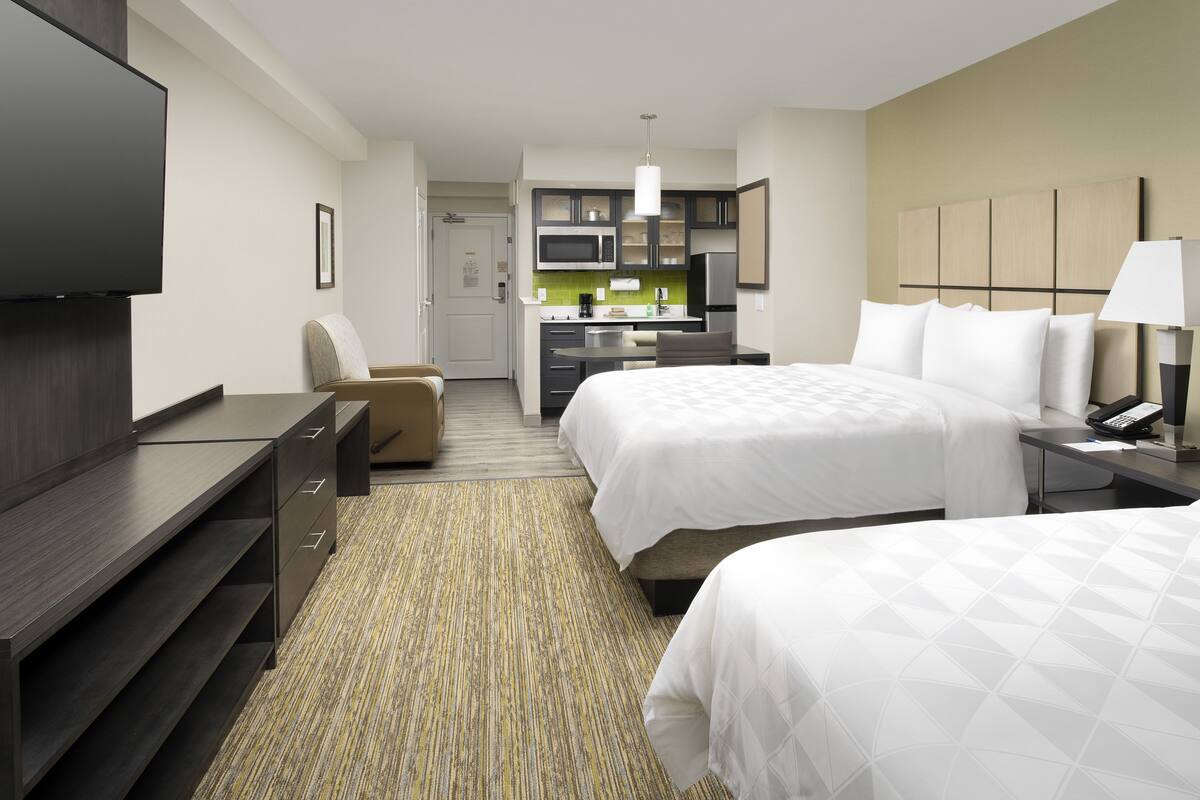 Habitación de hotel con dos camas, un escritorio, televisión, kitchenette y baño.