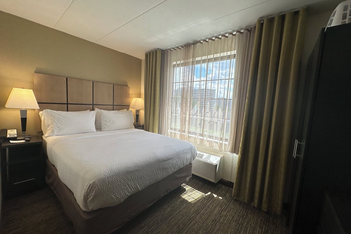 Habitación de hotel con una cama grande, dos lámparas de noche, una ventana con cortinas y un radiador.